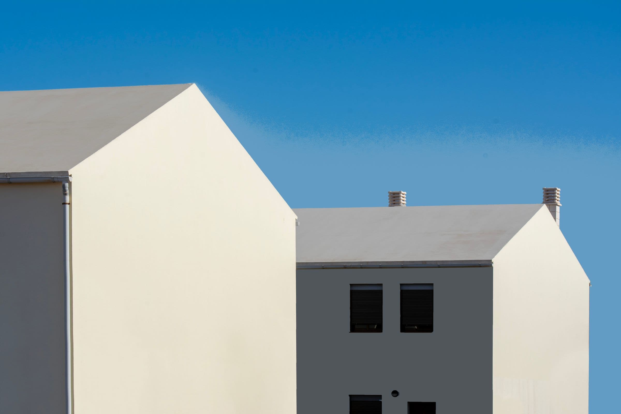 Zwei versetzte, schlichte Satteldachhäuser vor blauem Himmel
